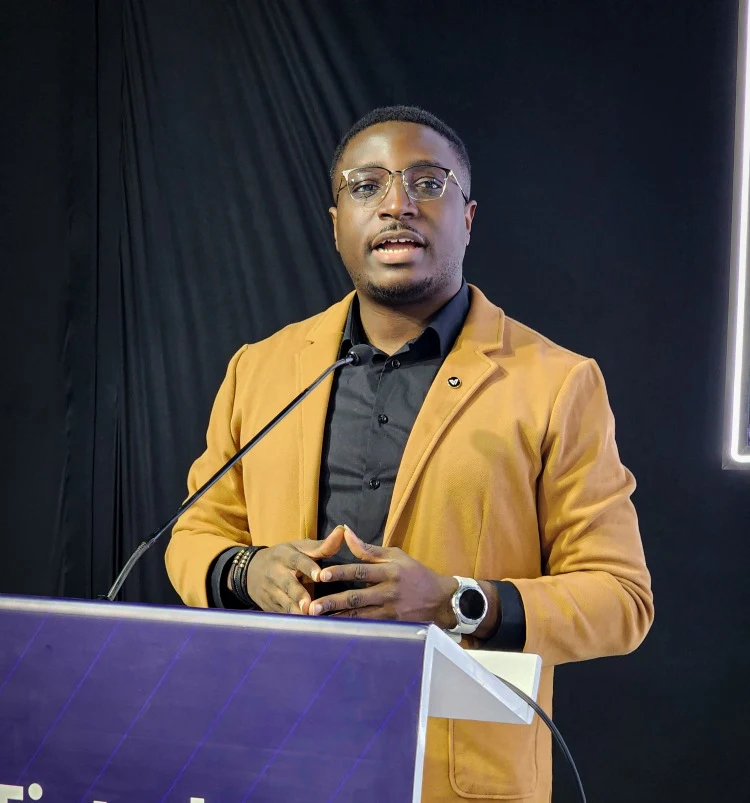Kenny Nwokoye in a gold blazer speaking at a lectern